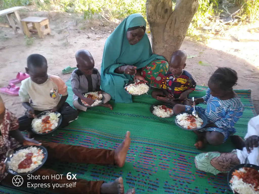 Family enjoying a meal outdoors on mat.